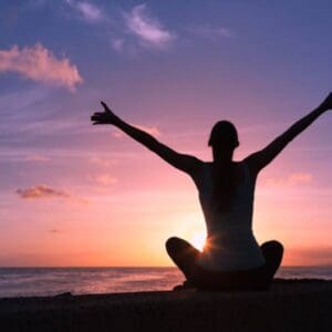 A person sitting on the beach with their arms in the air.