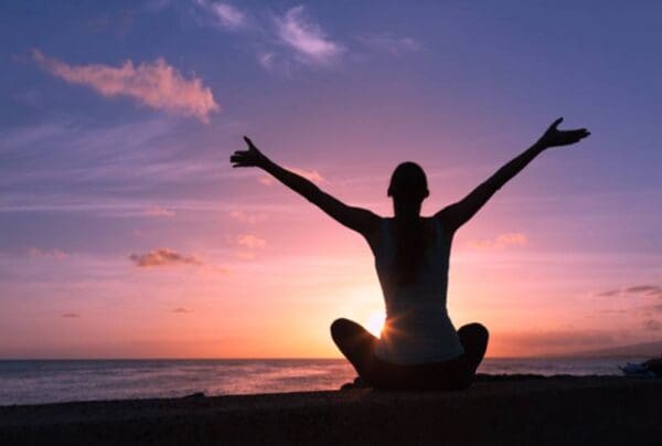 A person sitting on the beach with their arms in the air.