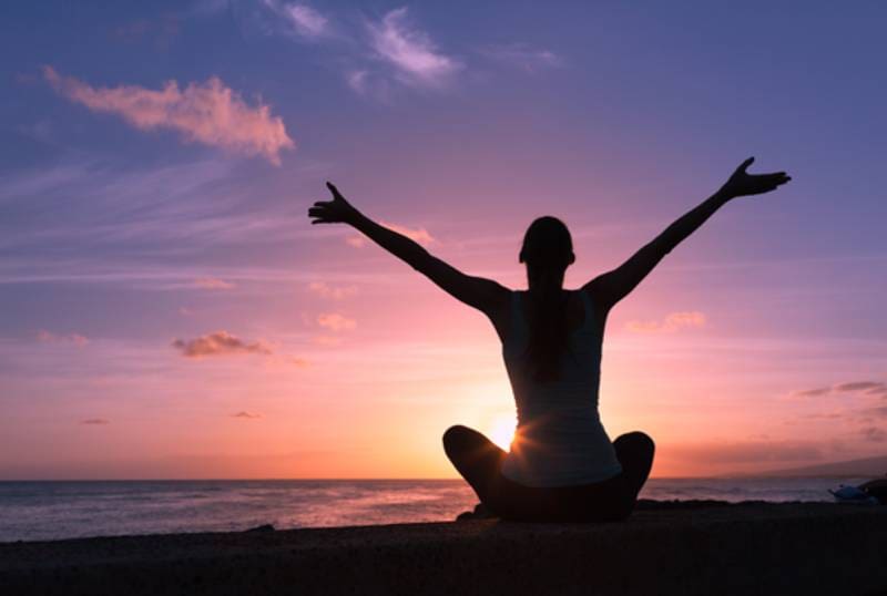 A person sitting on the beach with their arms in the air.