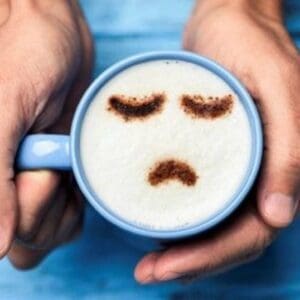 A person holding a cup of coffee with a sad face drawn on it.