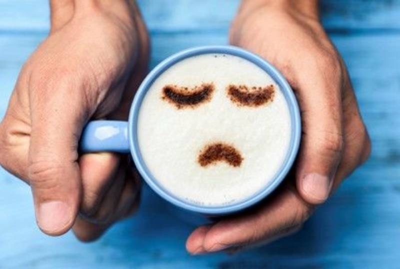 A person holding a cup of coffee with a sad face drawn on it.