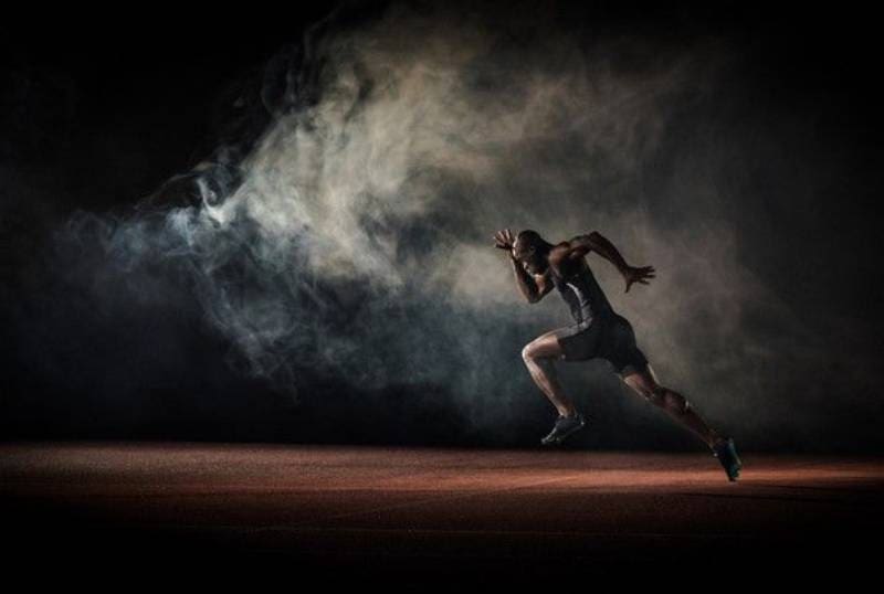 A man running in the dark with smoke coming from behind him.