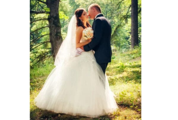 A bride and groom kissing in the woods