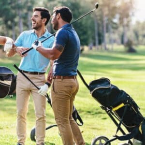 Two men are playing golf and one is holding a bag.